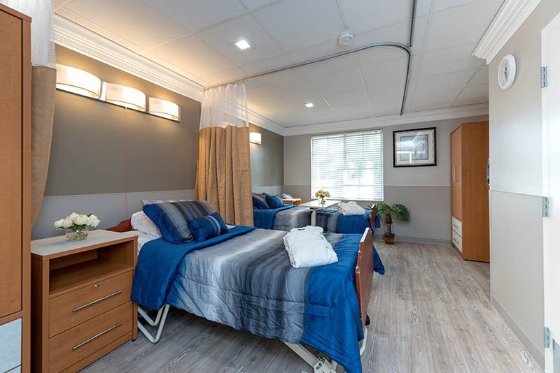 A modern hospital room with twin beds, blue bedding, and a dividing curtain.