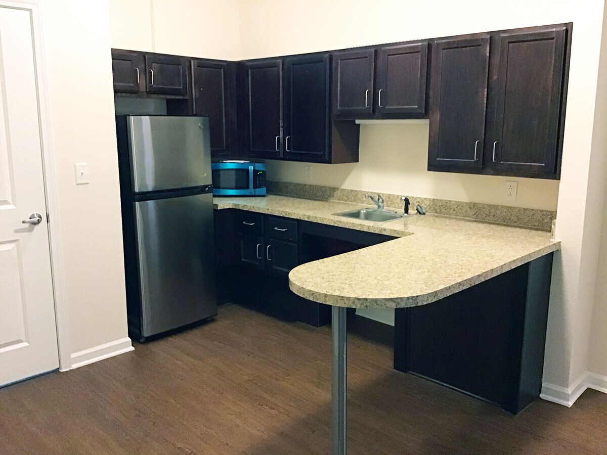 A modern kitchen with dark cabinets and a stainless steel refrigerator.