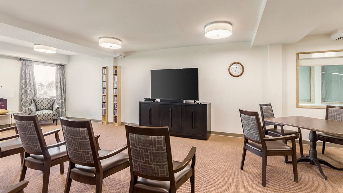 A cozy living room with a television, several chairs, a shelf, and a clock on the wall.