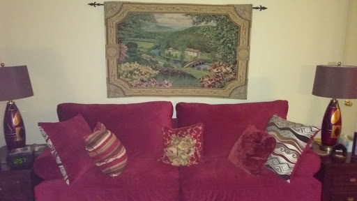 A cozy living room setup featuring a red couch adorned with decorative pillows and a beautiful tapestry hanging above.