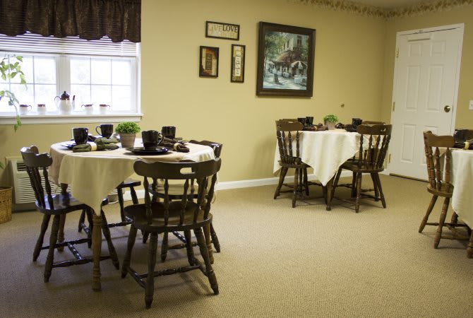 A cozy dining room with neatly set tables and wooden chairs, adorned with wall decorations and a window providing natural light.