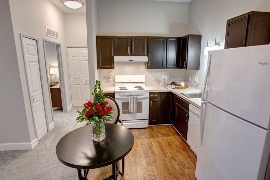 A modern kitchen in an apartment with dark cabinetry, a white stove and refrigerator, and a small dining table with red roses.