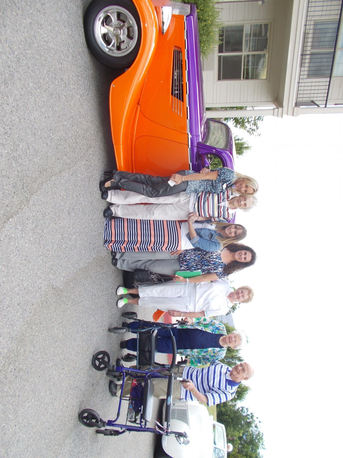 A group of people stand beside a brightly colored classic car in a residential area.