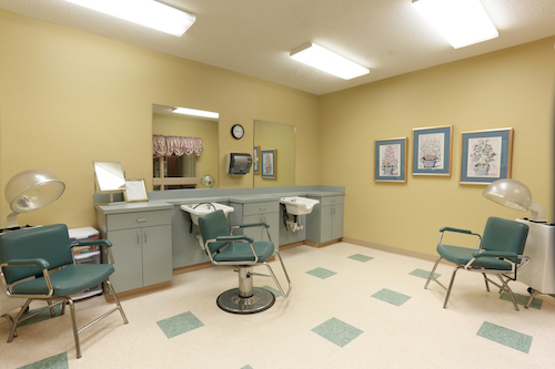 A tidy and well-lit barber shop with green chairs and a minimalist design.