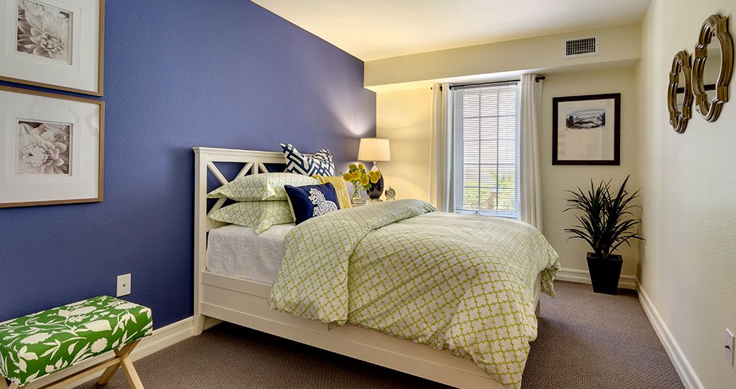 A cozy bedroom with a blue accent wall, neatly made bed, and soft lighting.