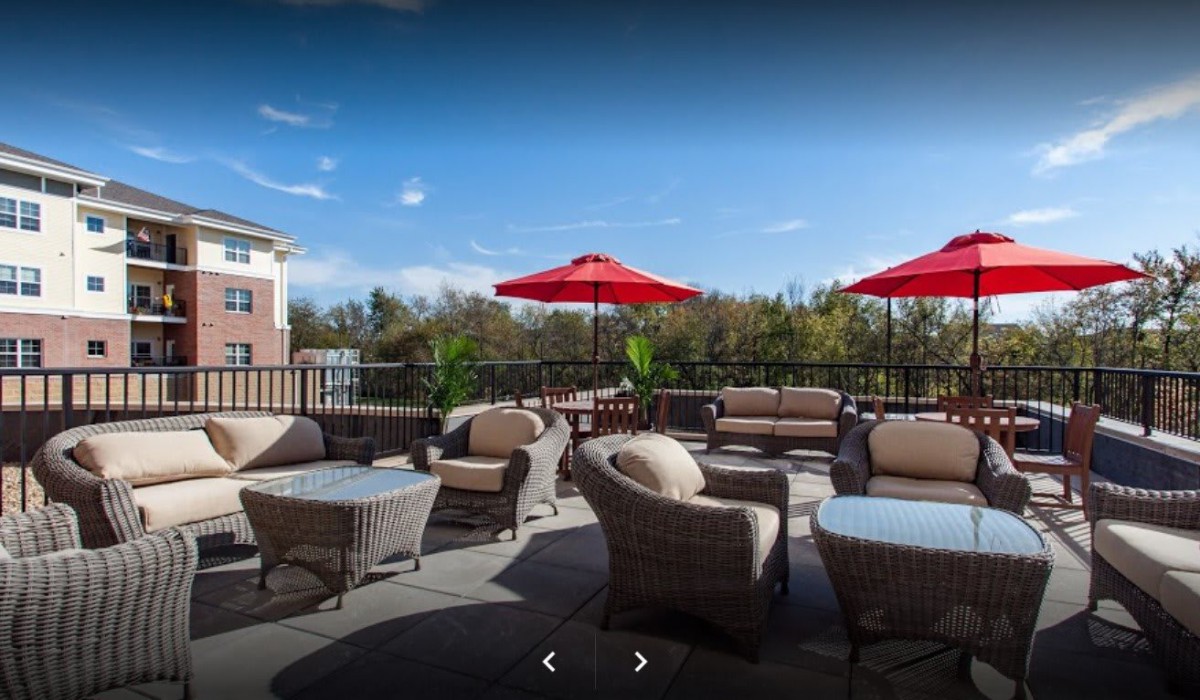 A cozy outdoor patio featuring wicker furniture and red umbrellas under a clear blue sky.