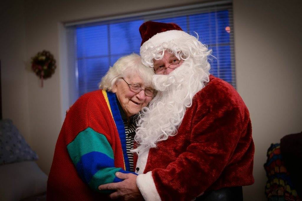 An elderly woman joyfully embraces a person dressed as Santa Claus during the holiday season.