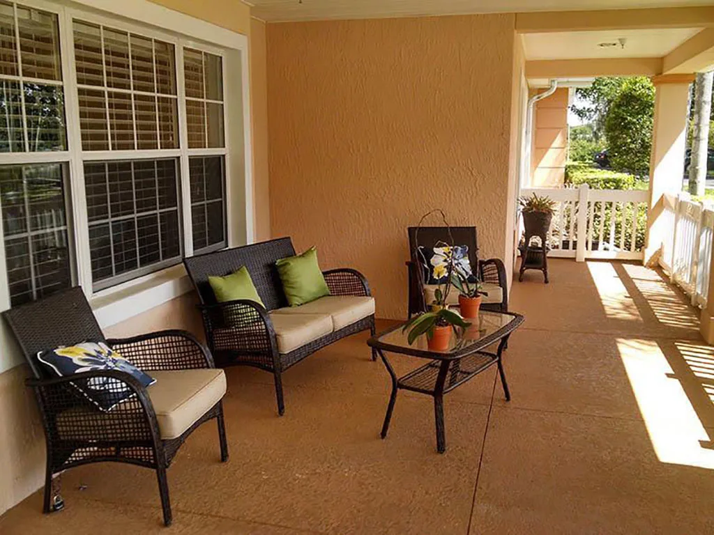 A cozy porch with comfortable wicker seating and a glass-top table adorned with potted plants.