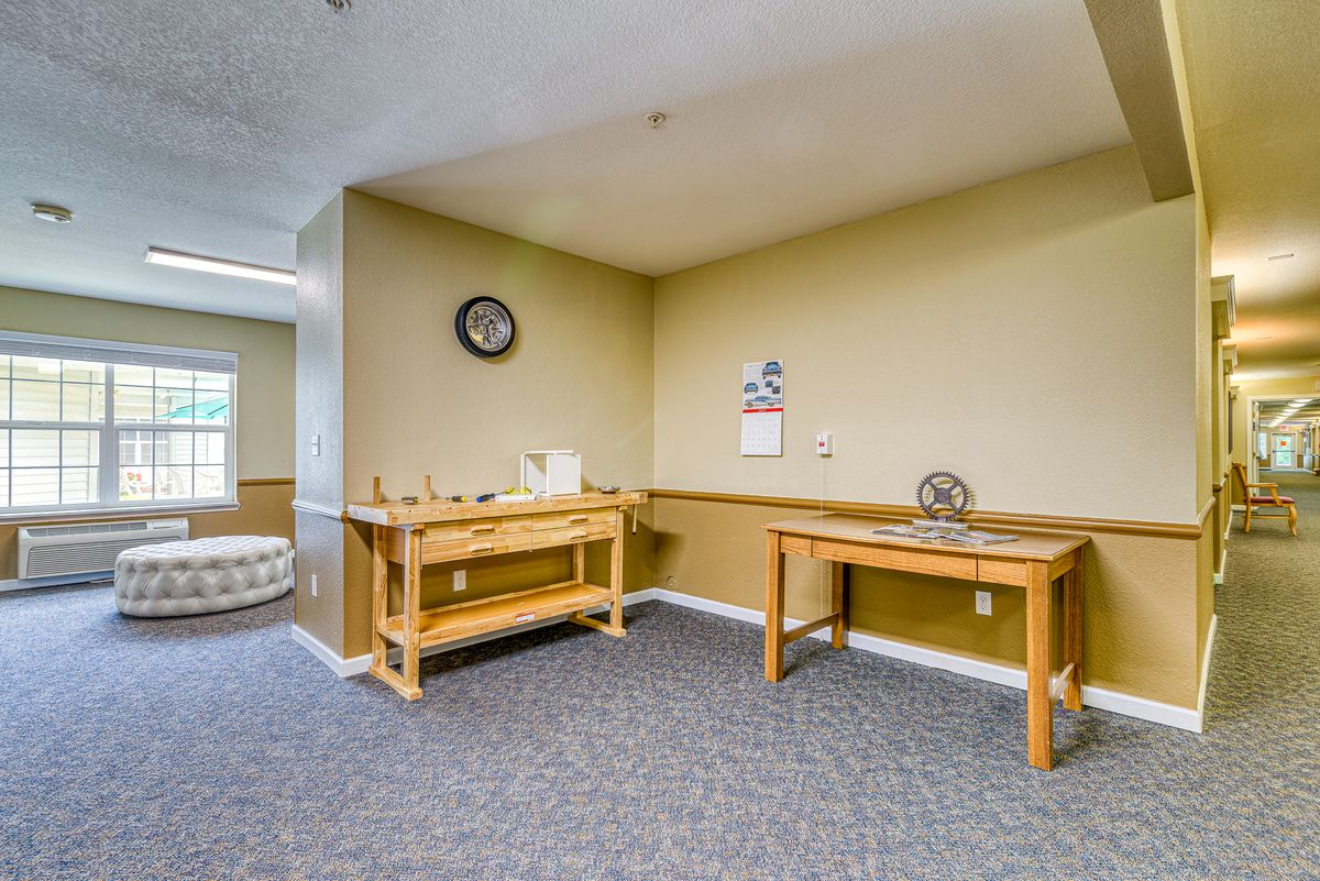 A simple waiting area with two wooden tables, a clock on the wall, and carpeted flooring.