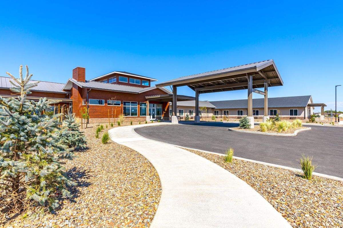 A modern building with a covered entrance and surrounding landscape under a clear blue sky.
