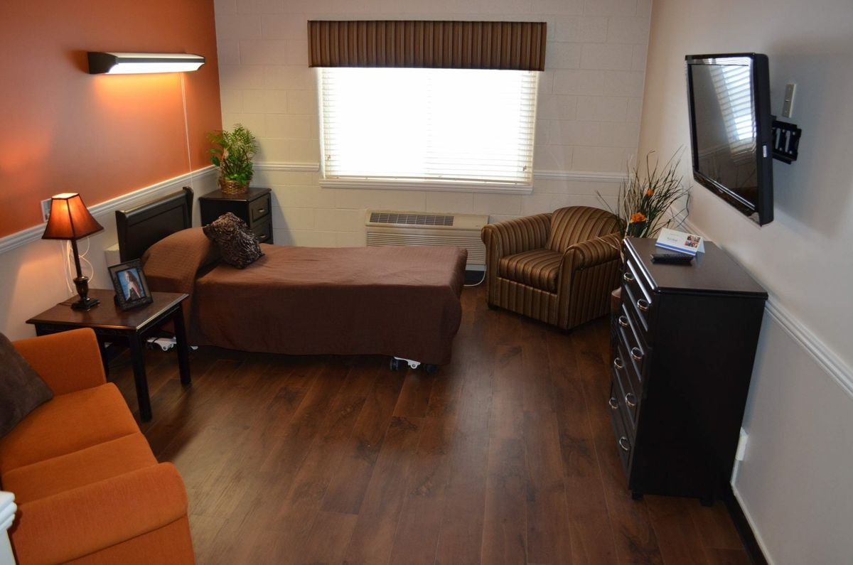 A cozy bedroom with a single bed, armchair, television, and dresser on wood flooring.