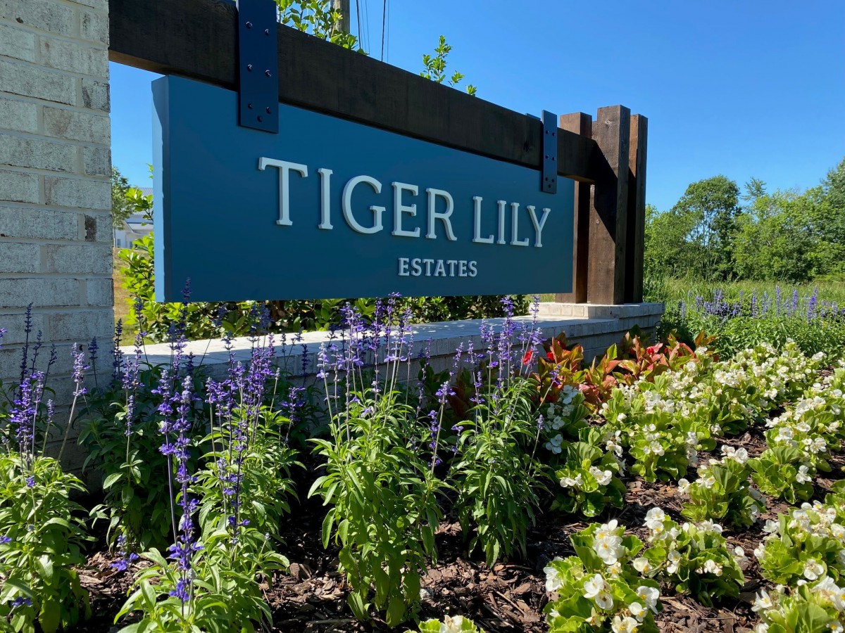 Entrance sign for Tiger Lily Estates surrounded by vibrant flowers and greenery.