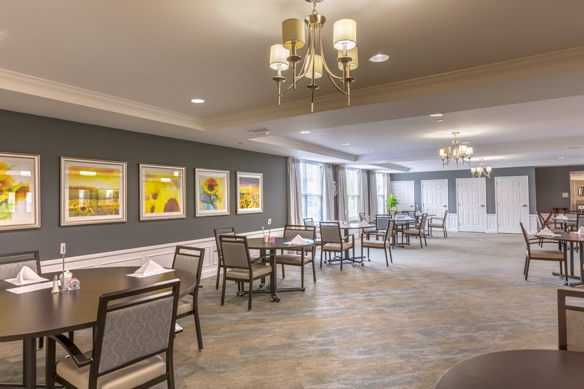 A bright dining area with neatly arranged tables and chairs, adorned with elegant lighting fixtures and colorful wall art.