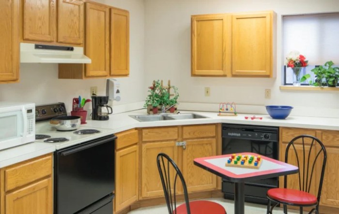 A cozy kitchen with wooden cabinets, a countertop with appliances, and a small table set with a chessboard.