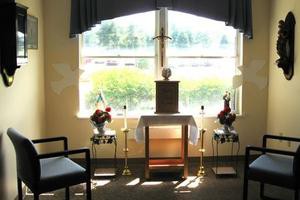 A small chapel with an altar, featuring candles and flowers by a window.