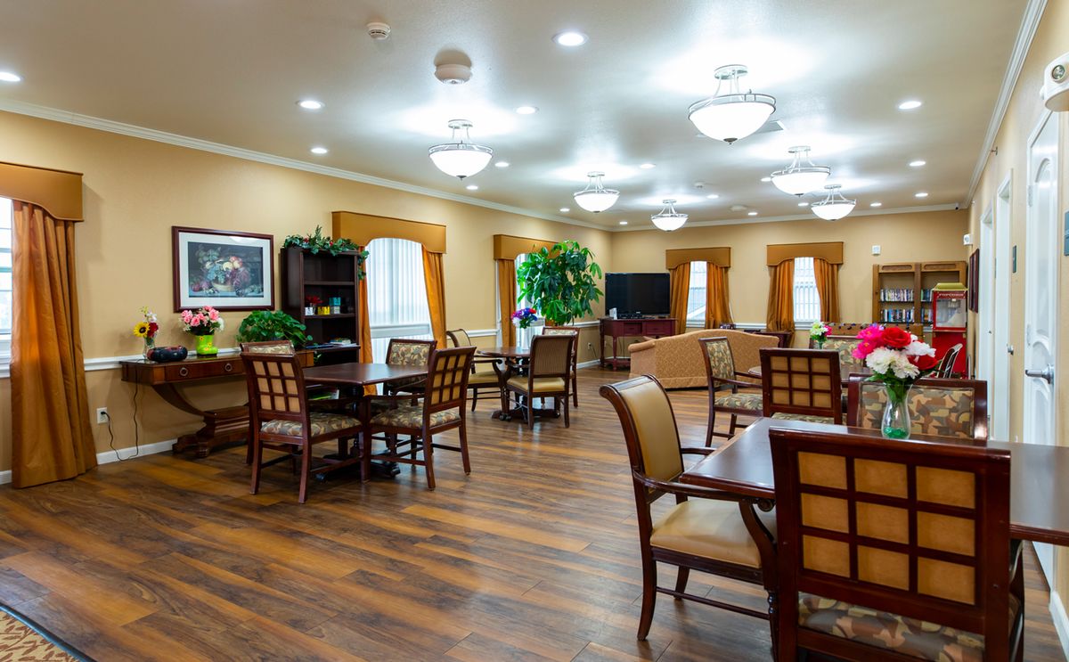A well-lit dining area with wooden floors, tables, and chairs arranged neatly throughout the room.