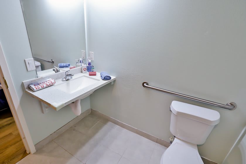 A clean bathroom with a sink, mirror, and toilet equipped with a grab bar.
