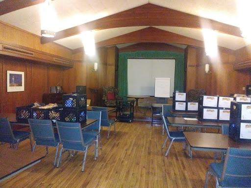 A spacious meeting room with chairs and tables set up for a session, featuring a whiteboard at the front.