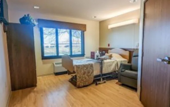 A well-lit hospital room with a bed, chair, and large window.