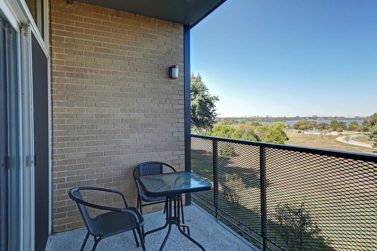 A balcony with two chairs and a glass table overlooking a scenic landscape.