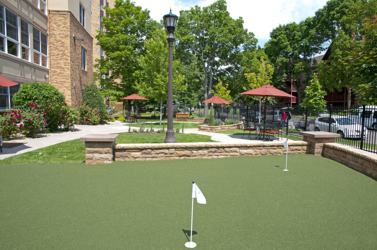 An outdoor putting green with trees and umbrellas in the background.