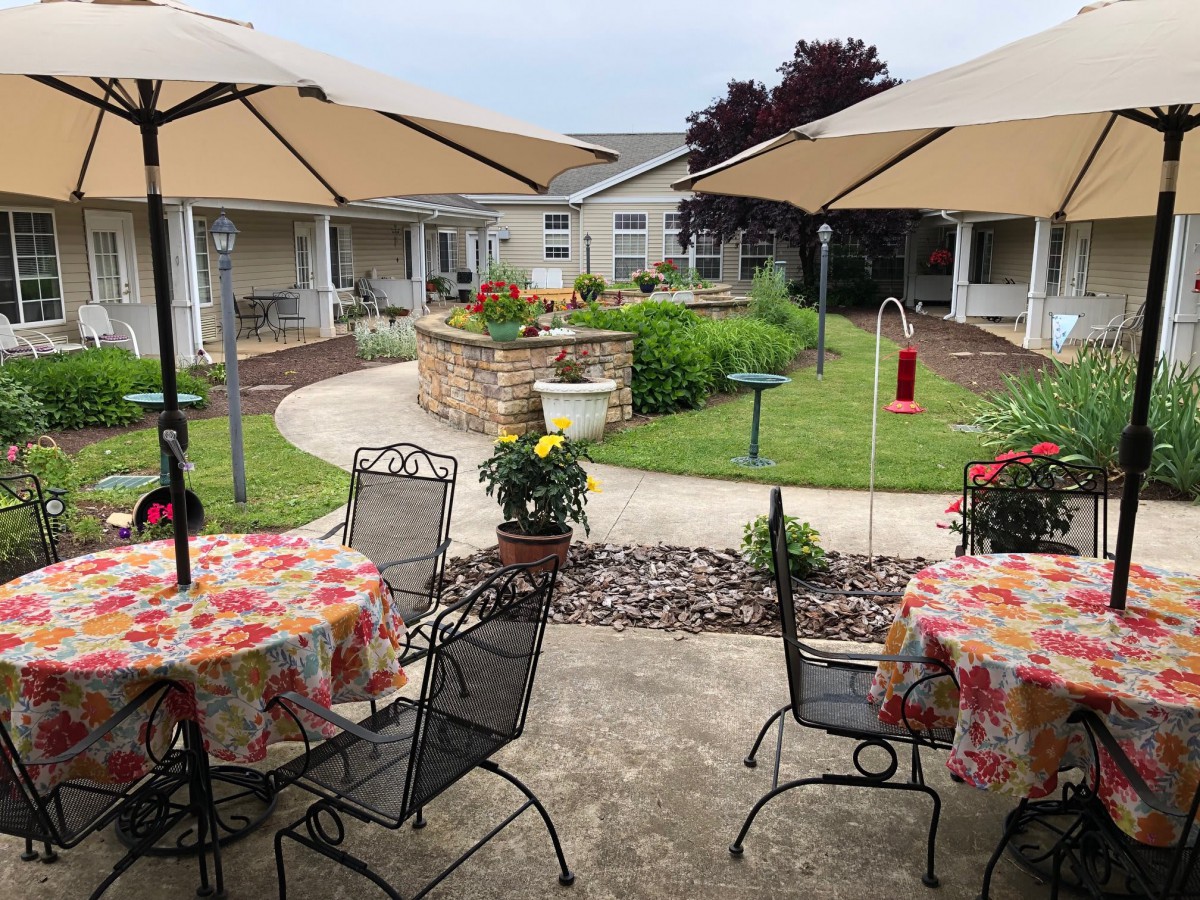 A charming courtyard with tables and umbrellas overlooking a garden.