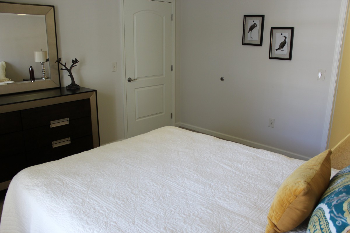 A minimalist bedroom with a simple bed, two bird-themed wall pictures, and a small dresser.