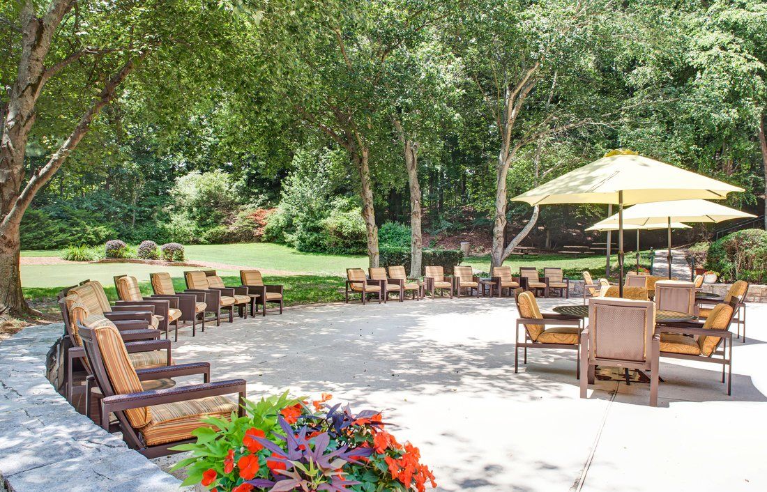 A beautiful outdoor patio area with chairs, tables, and umbrellas surrounded by lush greenery and colorful flowers.