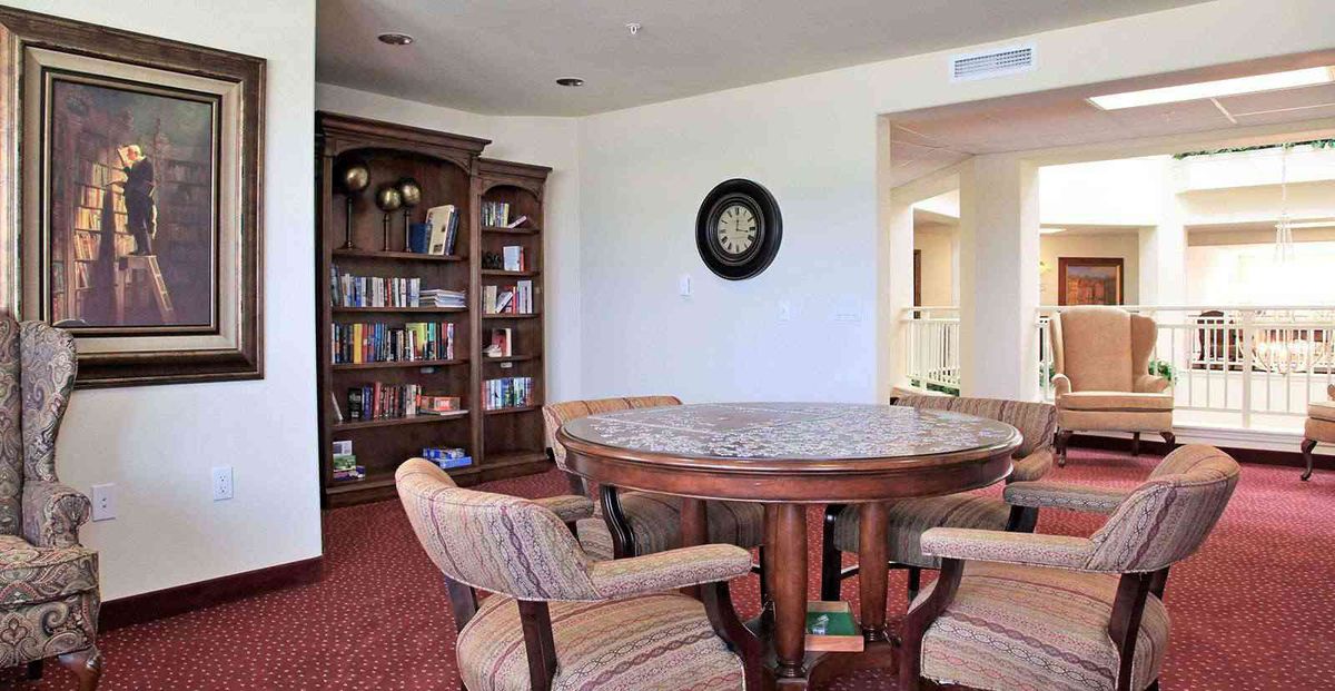 A cozy library room featuring a round table surrounded by chairs and a bookshelf filled with books.