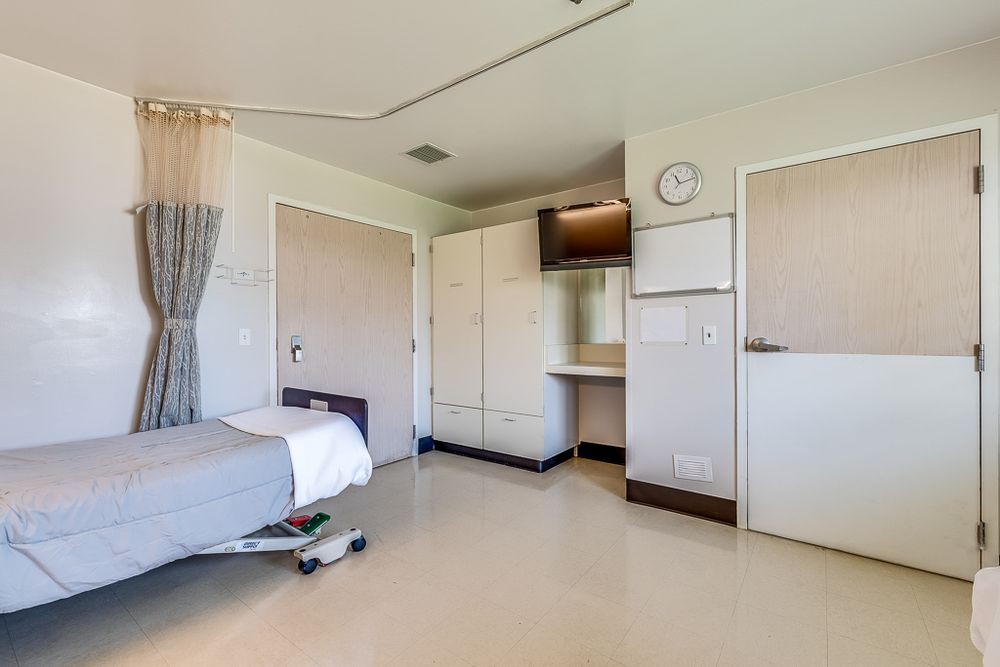 A clean and empty hospital room with a bed and medical equipment.