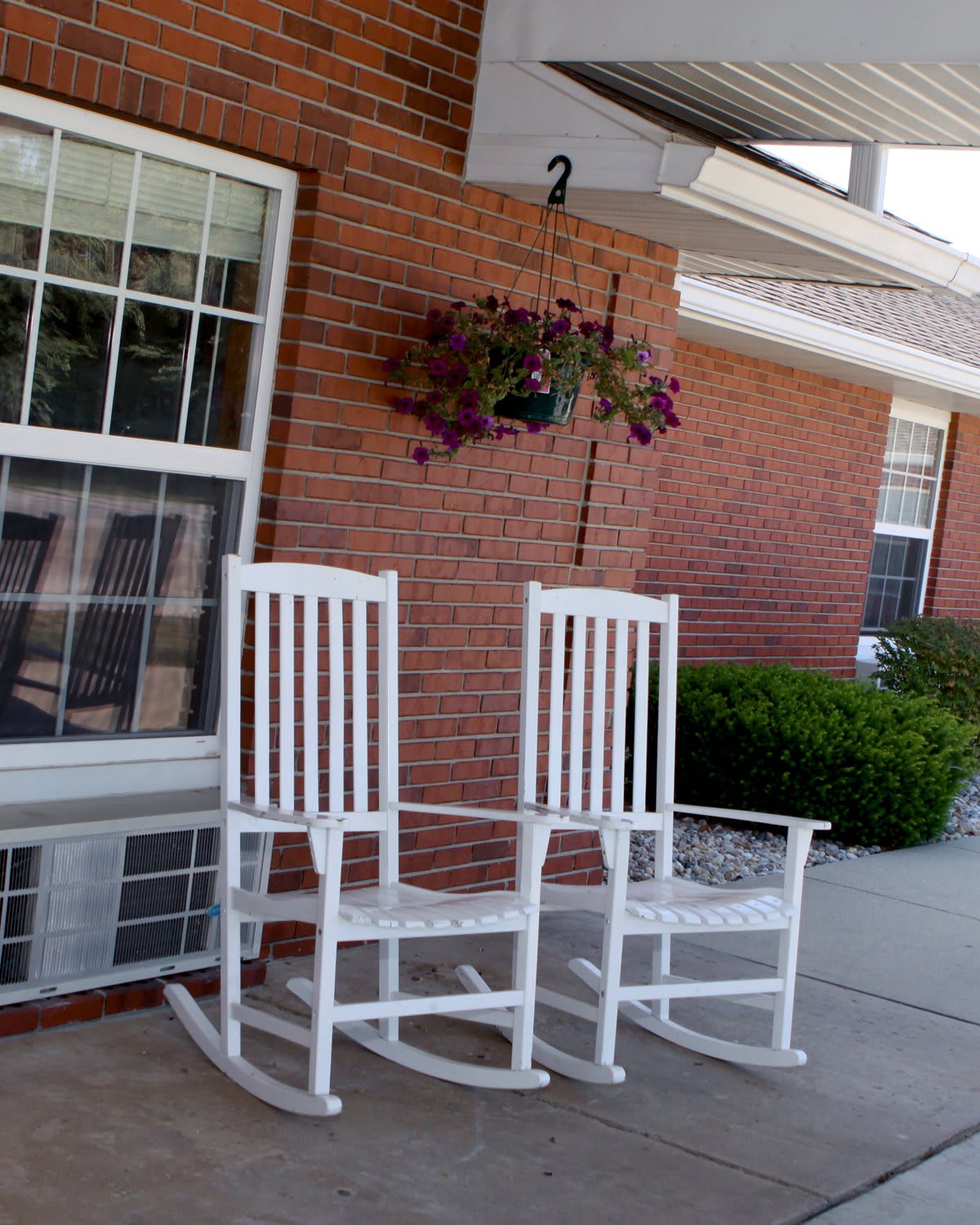 Two white rocking chairs on a porch with a hanging plant.