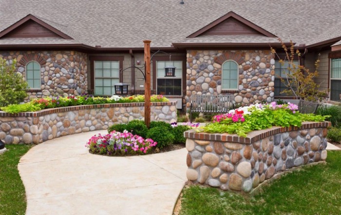 A beautifully landscaped house with a stone exterior and vibrant flower beds.