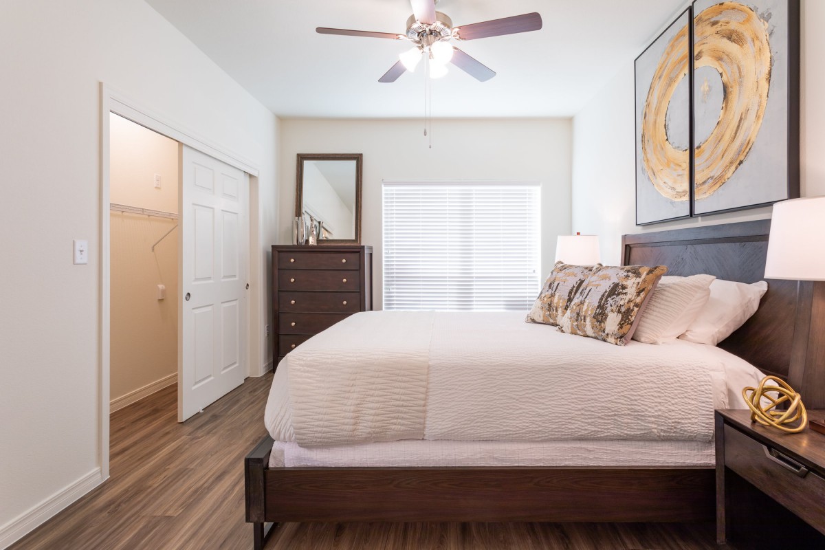 A modern bedroom with a neatly made bed, a dresser with a mirror, and a ceiling fan.