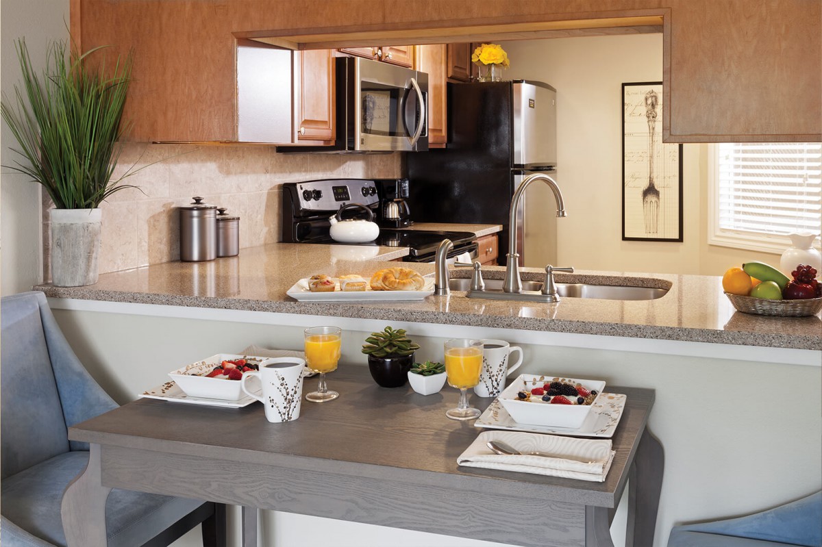 A modern kitchen with a breakfast bar set for two, featuring contemporary appliances and decor.