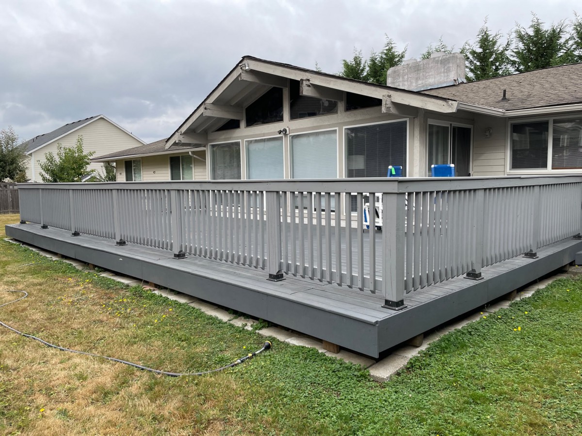 A wooden deck attached to the back of a house, featuring railings and overlooking a grassy backyard.