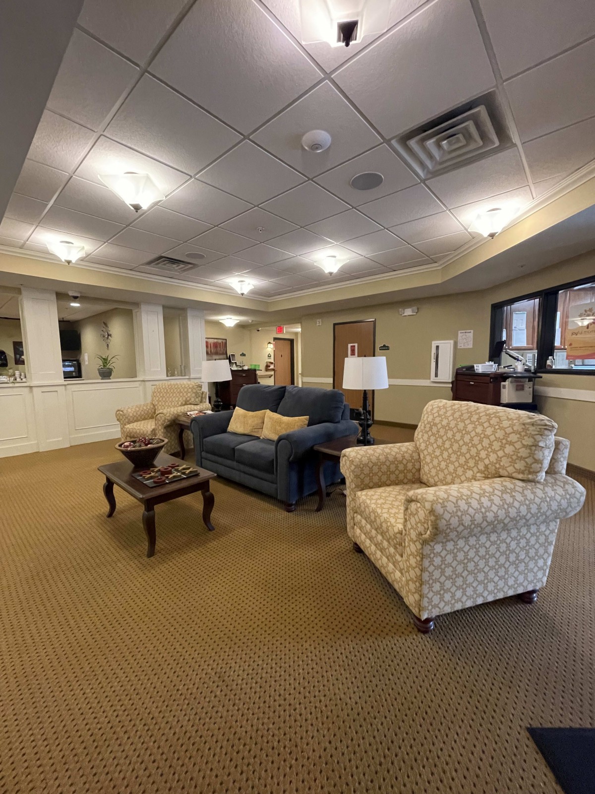 A cozy lobby area featuring a sofa, armchairs, coffee table, and lamps in a well-lit room.