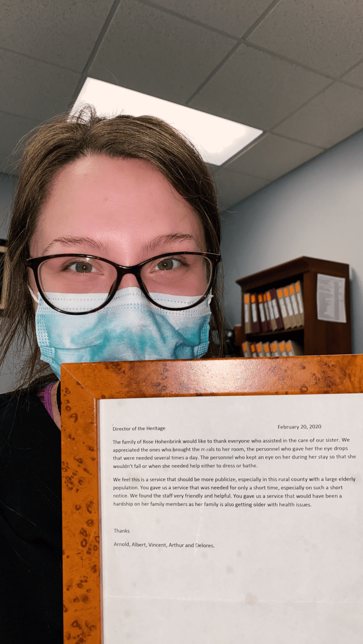 A person wearing glasses and a mask holds a framed document in an office setting.