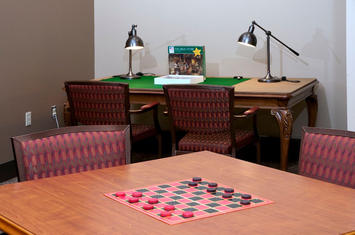 A cozy gaming area featuring a checkers board on the table, surrounded by chairs and lit by lamps.