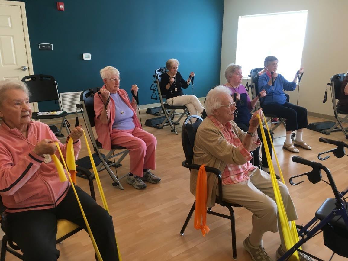 A group of seniors participating in a seated exercise class using resistance bands.