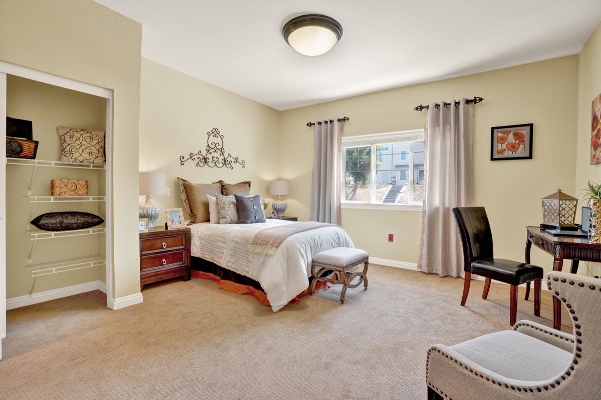 A well-decorated bedroom featuring a bed with pillows, nightstands with lamps, and a window with curtains.