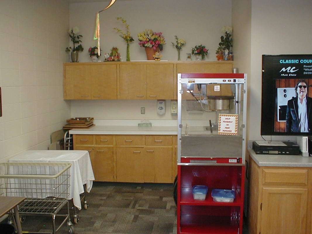 A kitchenette area featuring a popcorn machine, countertop with overhead cabinets, and decorative flowers.