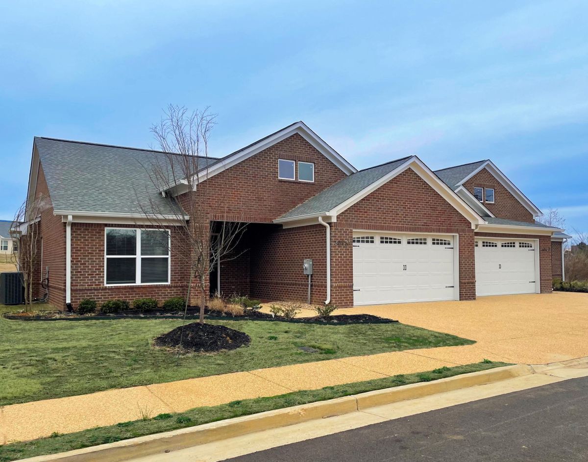 A suburban brick house with a three-car garage and a neatly maintained lawn.