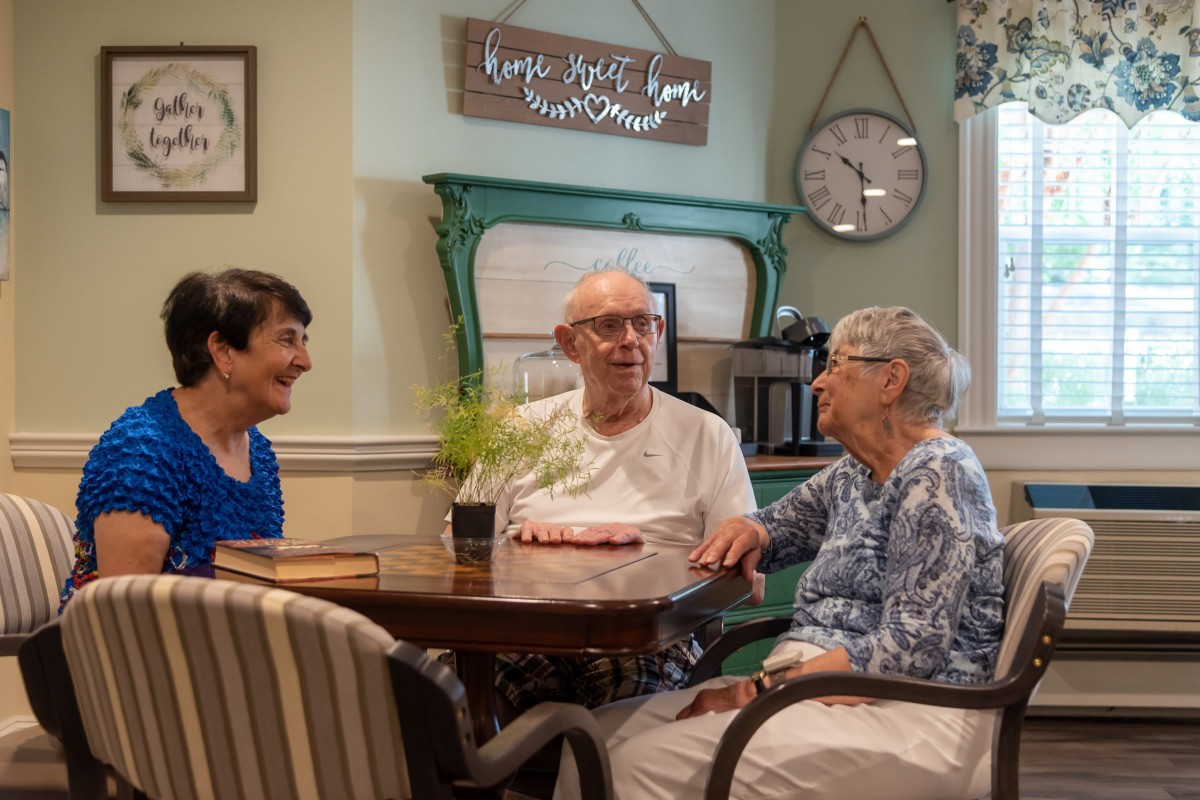 A group of three people sitting at a table, engaged in a friendly conversation in a cozy living room setting.