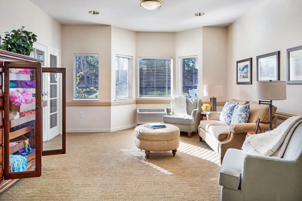 A cozy living room with ample natural light, featuring comfortable furniture and large windows.