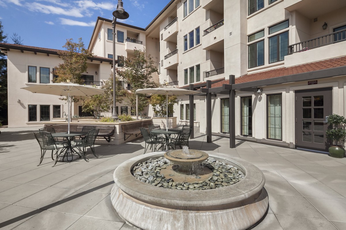 A modern apartment building courtyard featuring a central fountain and outdoor seating area.