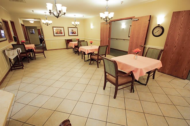 A spacious dining area with several tables and chairs, decorated with chandeliers and lit warmly, featuring a tiled floor.