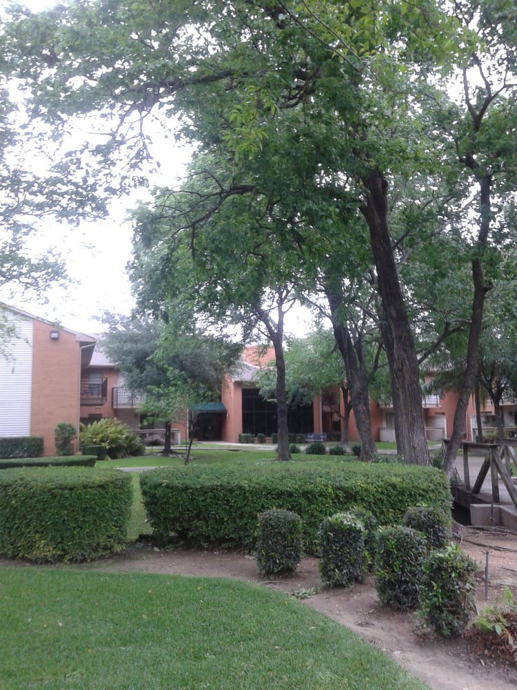 A view of an apartment complex surrounded by well-maintained landscaping and trees.