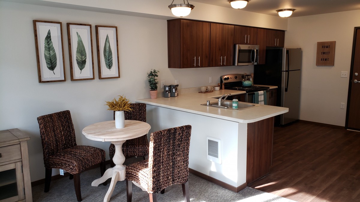 A modern kitchen with wooden cabinets, a small dining table, and stainless steel appliances.