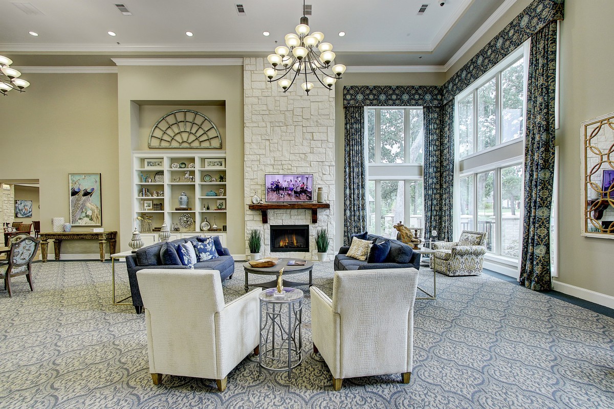 A luxurious living room with a chandelier, fireplace, and comfortable seating surrounded by large windows.