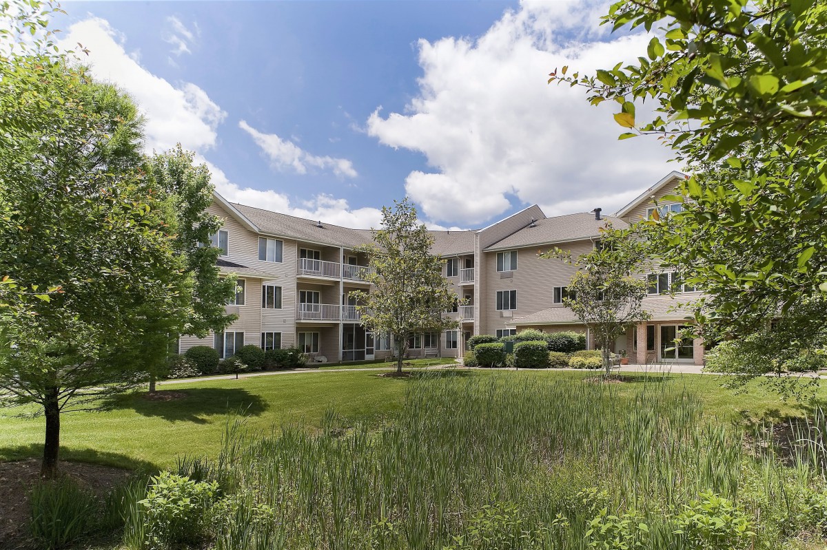 A residential apartment building surrounded by lush greenery and a well-maintained lawn under a partly cloudy sky.
